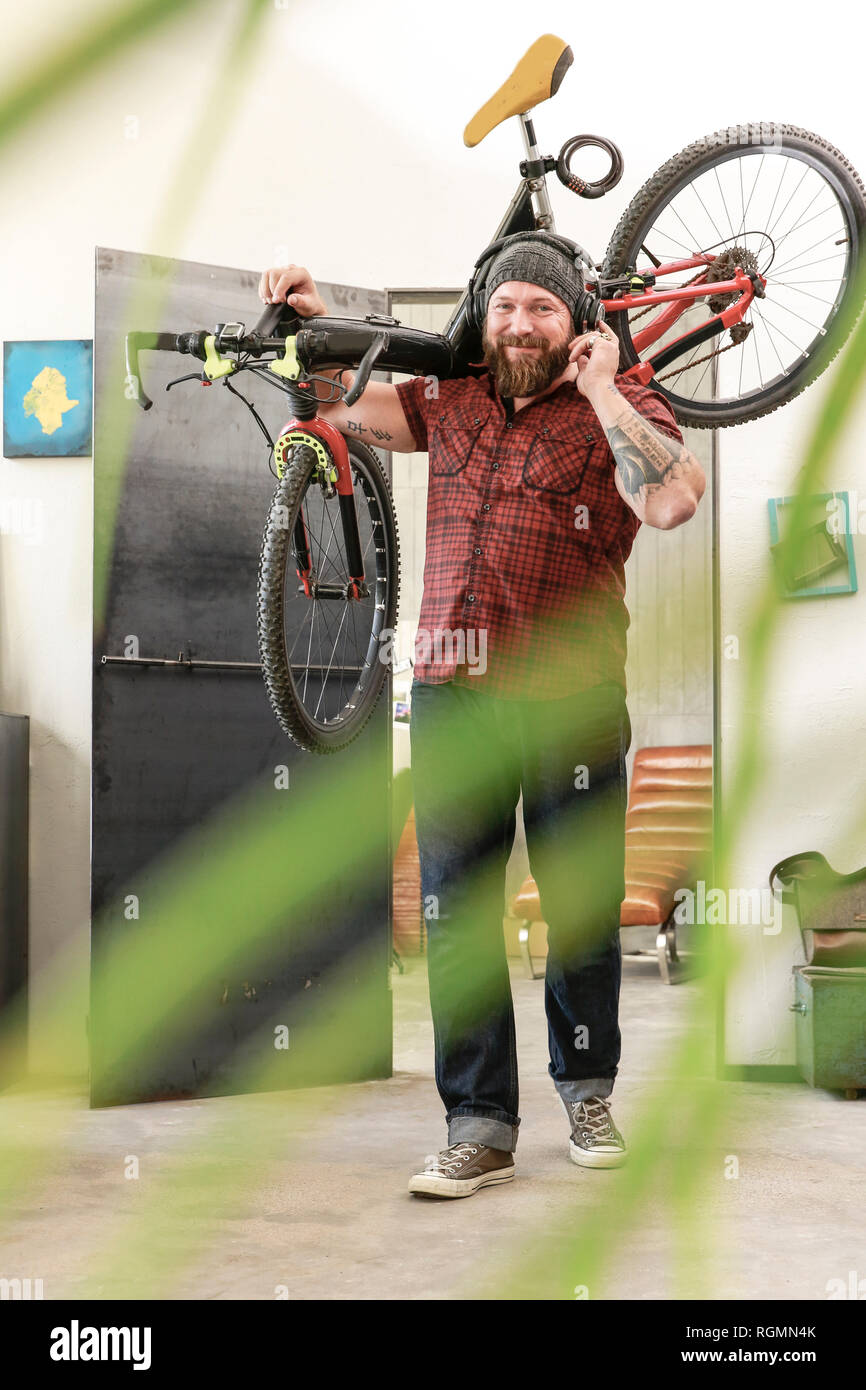 Ritratto di uomo sorridente che indossano le cuffie che trasportano in bicicletta in ufficio Foto Stock