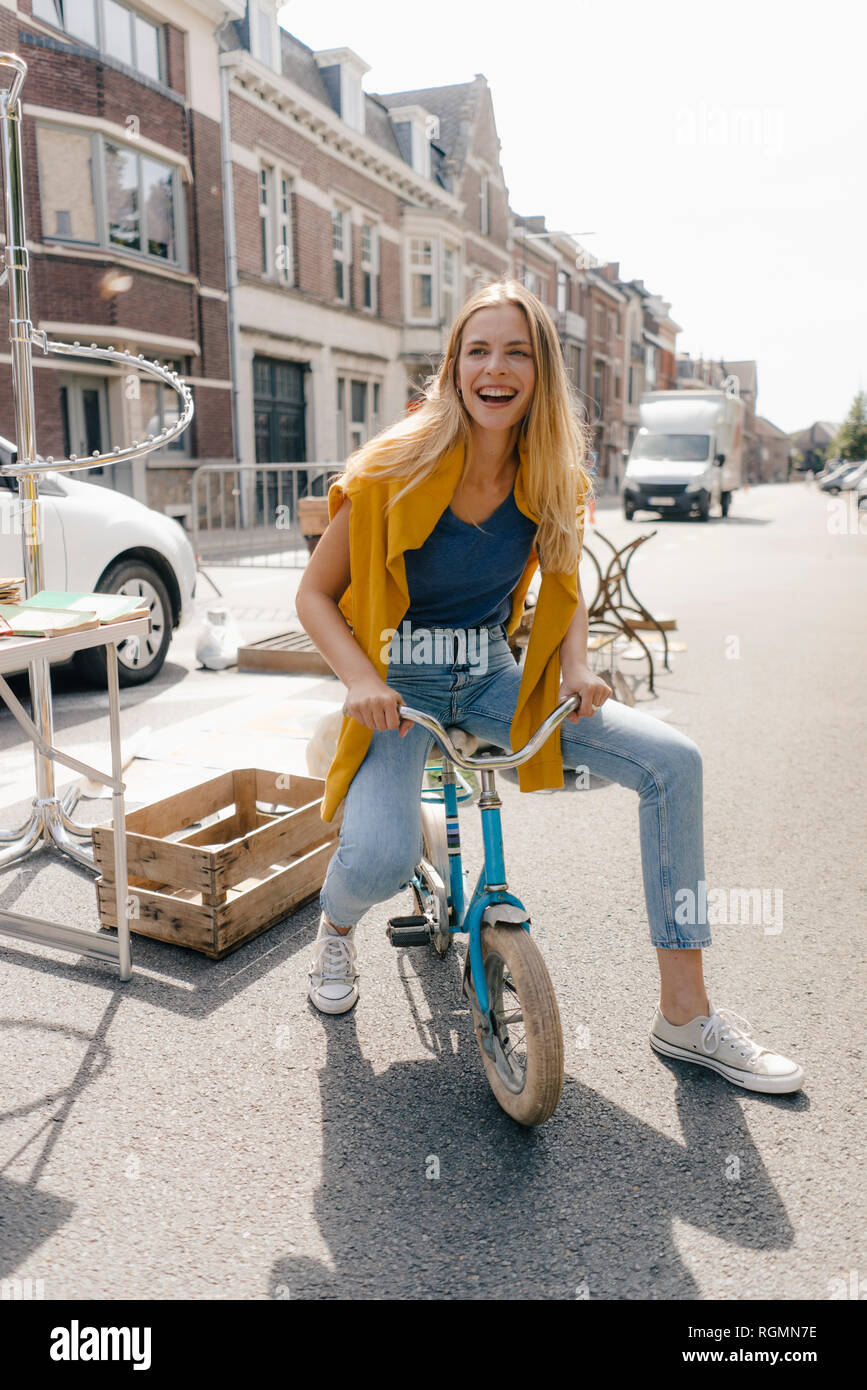 Belgio, Tongeren, felice giovane donna su un bambini bicicletta su un antico mercato delle pulci Foto Stock
