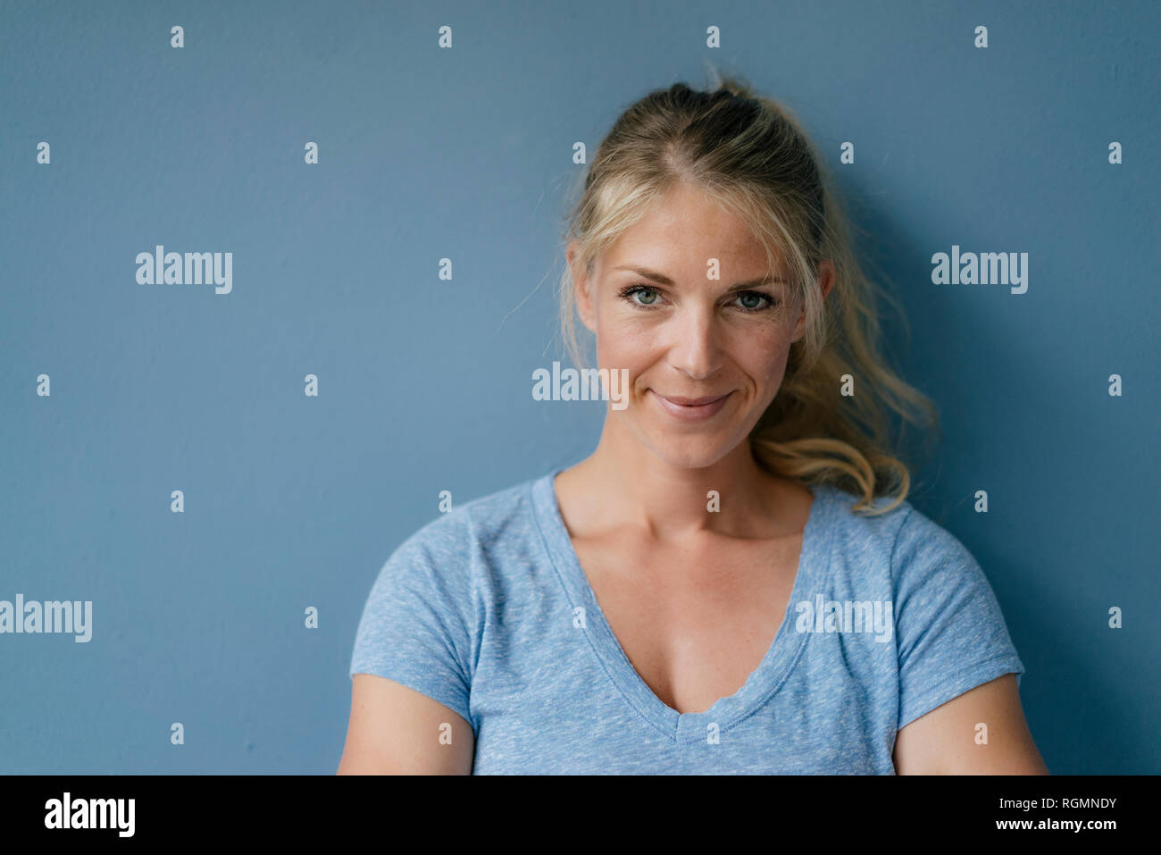 Ritratto di sorridere donna bionda in piedi alla parete blu Foto Stock