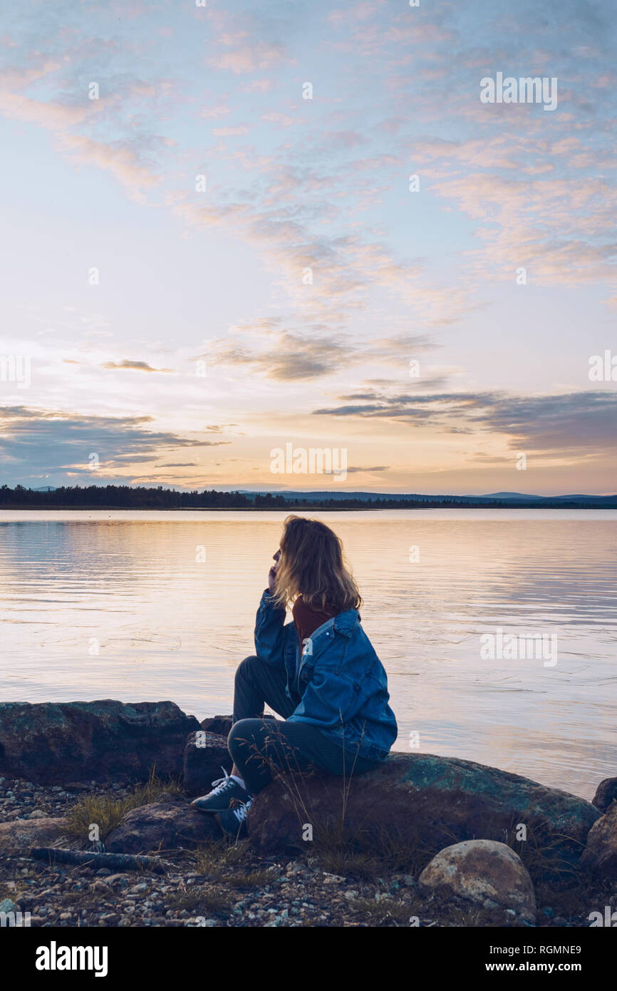 Giovane donna seduta al lago Inari, guardando a vista, Finlandia Foto Stock