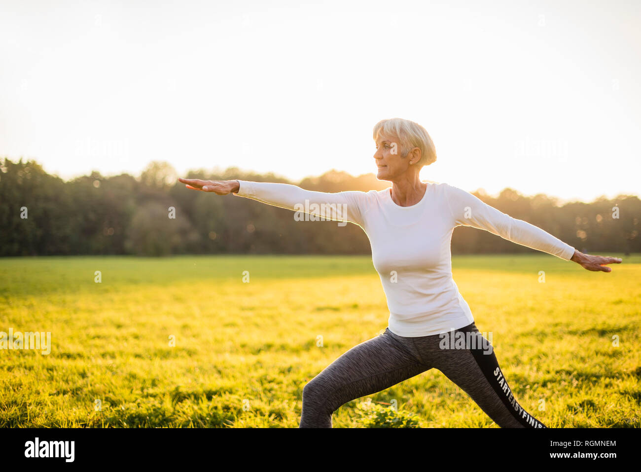 Senior donna fare yoga sul prato rurale al tramonto Foto Stock
