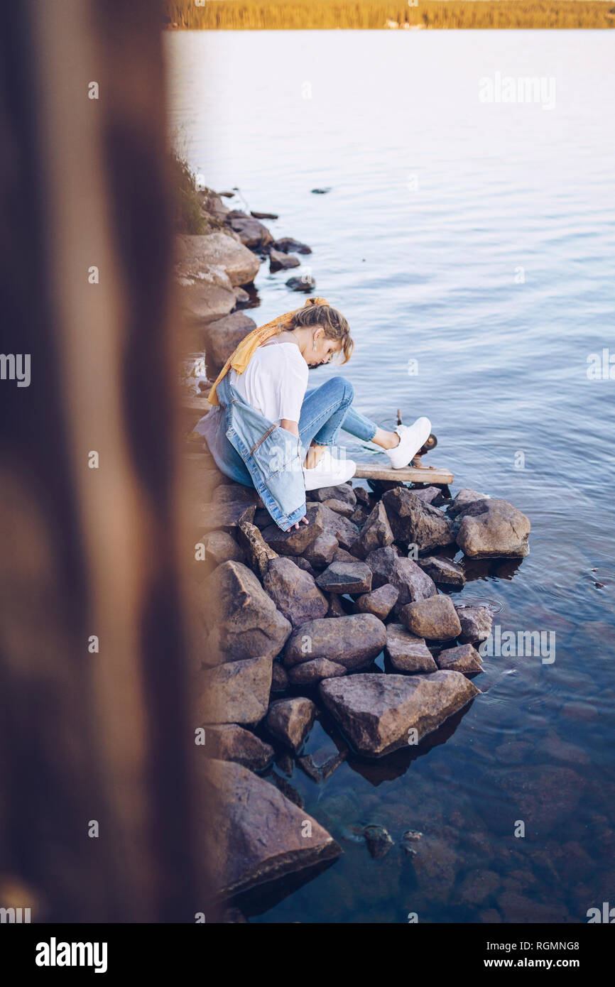 La Svezia, Lapponia, pensieroso giovane donna seduta a bordo d'acqua Foto Stock