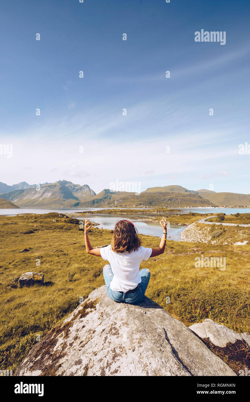 Norvegia Lofoten, vista posteriore della giovane donna seduta su una roccia a fare yoga Foto Stock