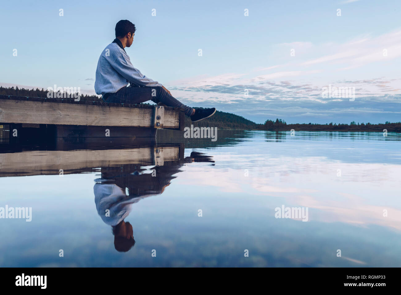 Giovane uomo seduto al lago Inari, guardando a vista, Finlandia Foto Stock