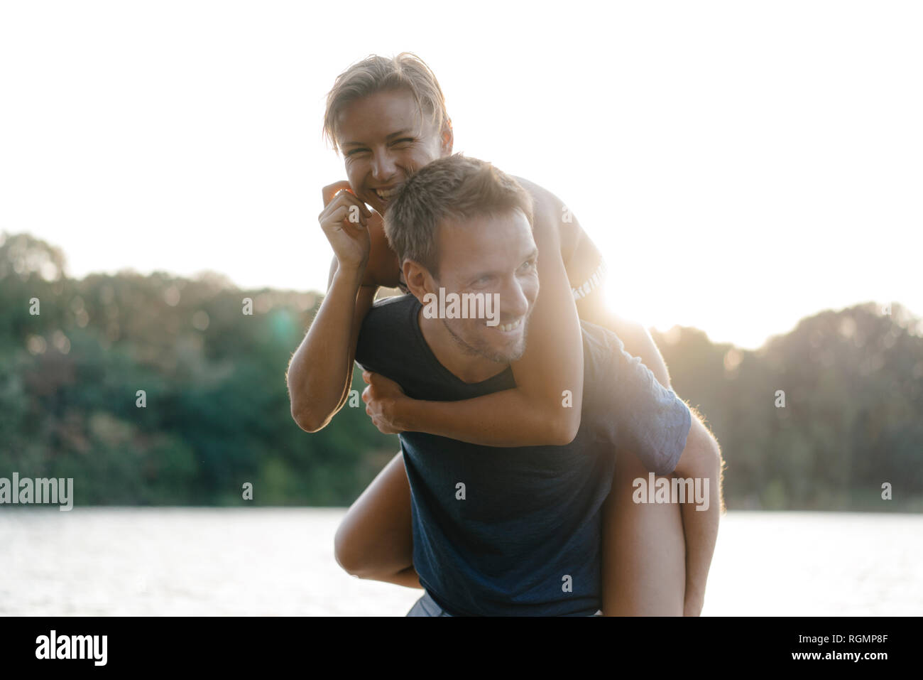 Felice l'uomo che porta la fidanzata sovrapponibile a un lago Foto Stock