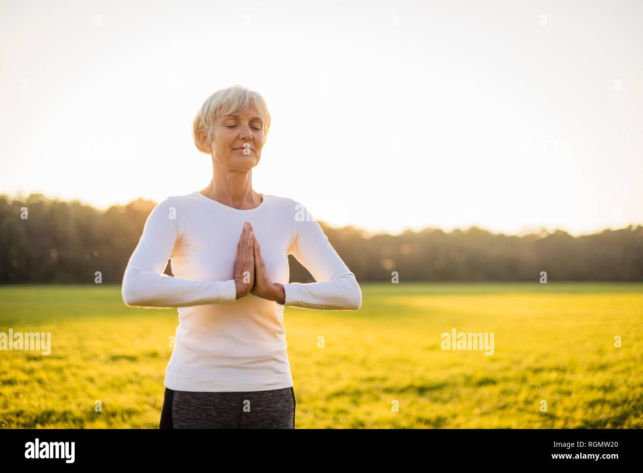 Senior donna fare yoga sul prato rurale al tramonto Foto Stock