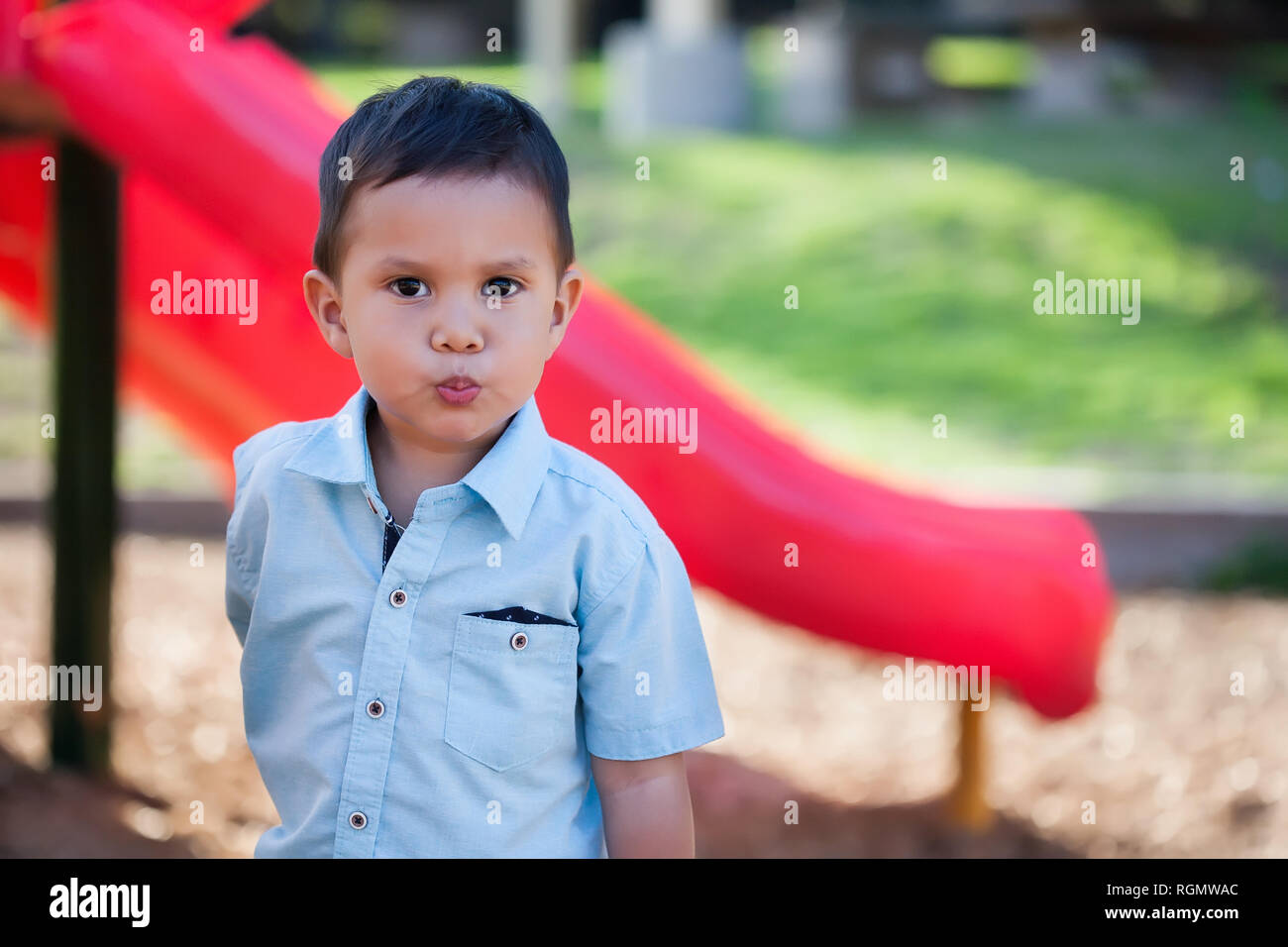 Un bel ragazzo in piedi di fronte a un parco giochi slitta con il broncio labbra e guardando sconvolto, moody o con un atteggiamento di scontro. Foto Stock