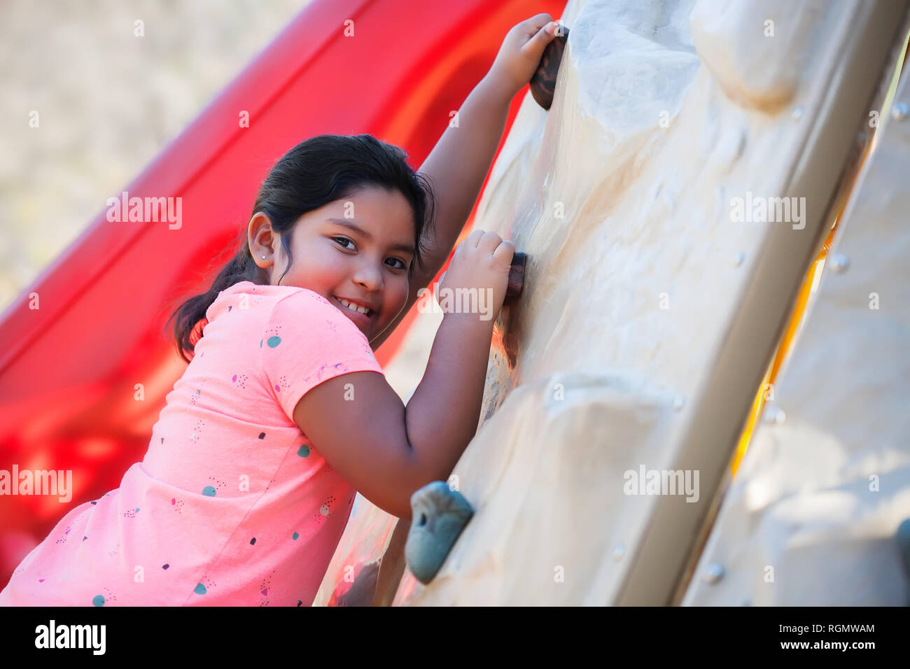 Giovane ragazza latino scalata di un parco giochi a parete e sorridente. Foto Stock