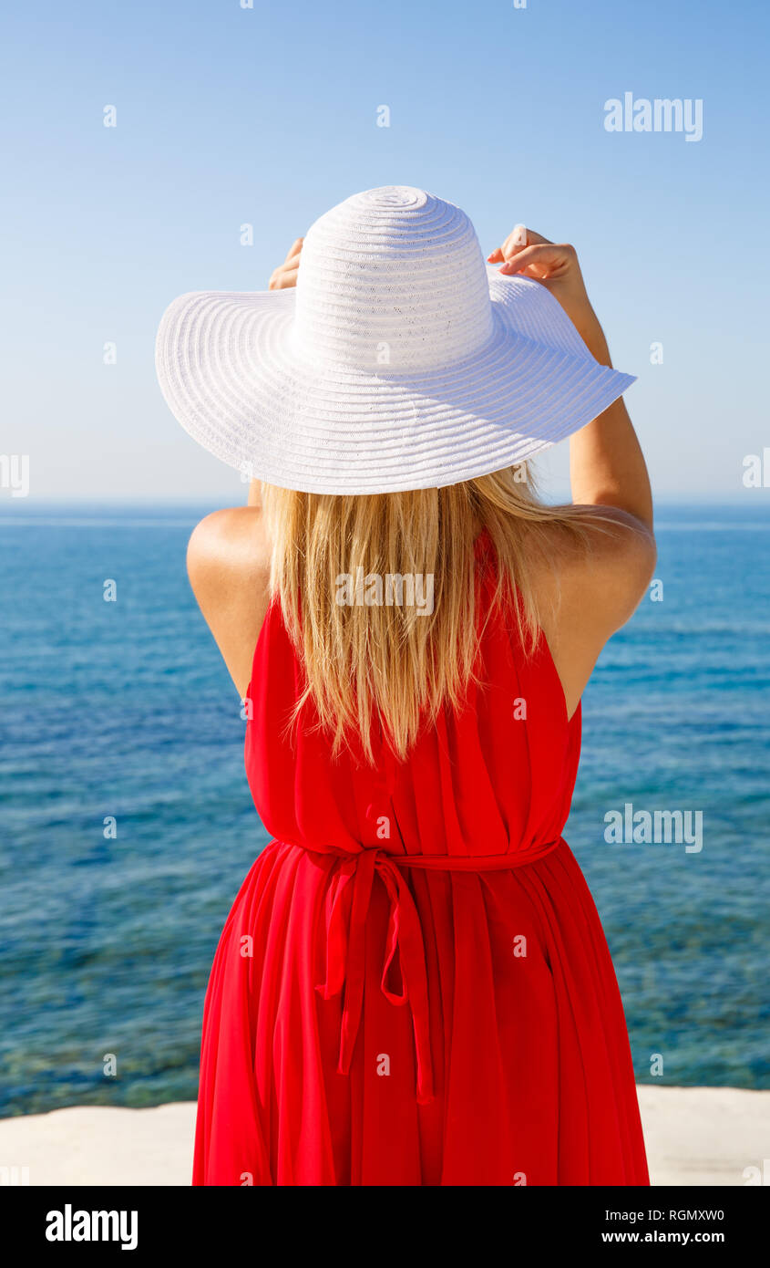 Donna bionda in abito rosso con il cappello bianco presso la spiaggia di Cipro. Foto Stock