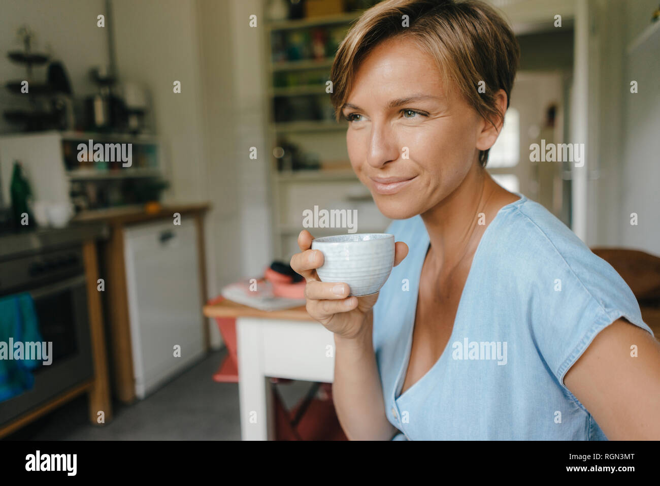 Donna sorridente a casa a bere tazza di caffè Foto Stock