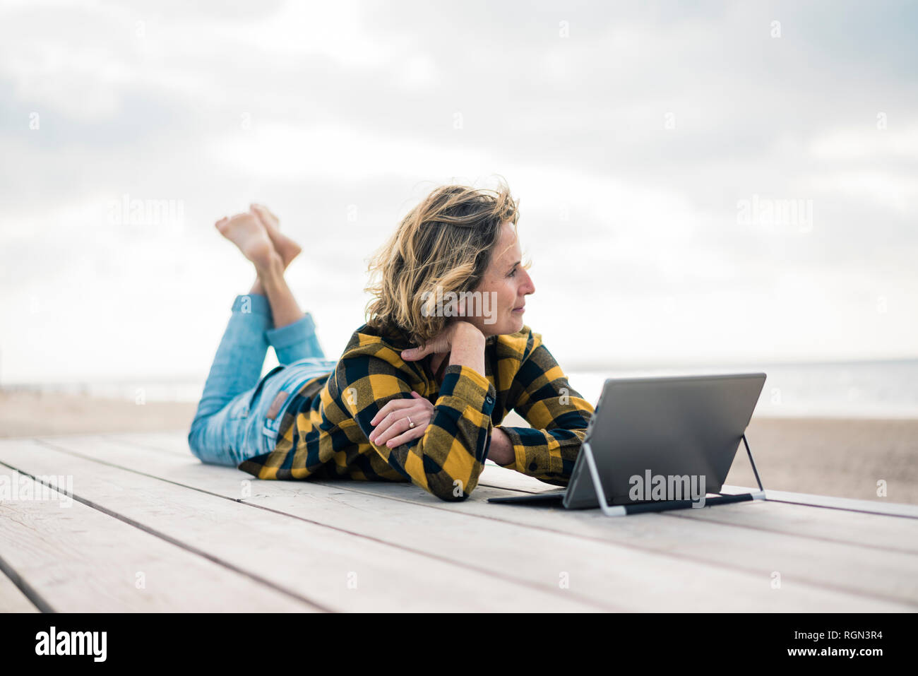 Donna matura giacente sul Boardwalk in spiaggia, utilizzando laptop Foto Stock