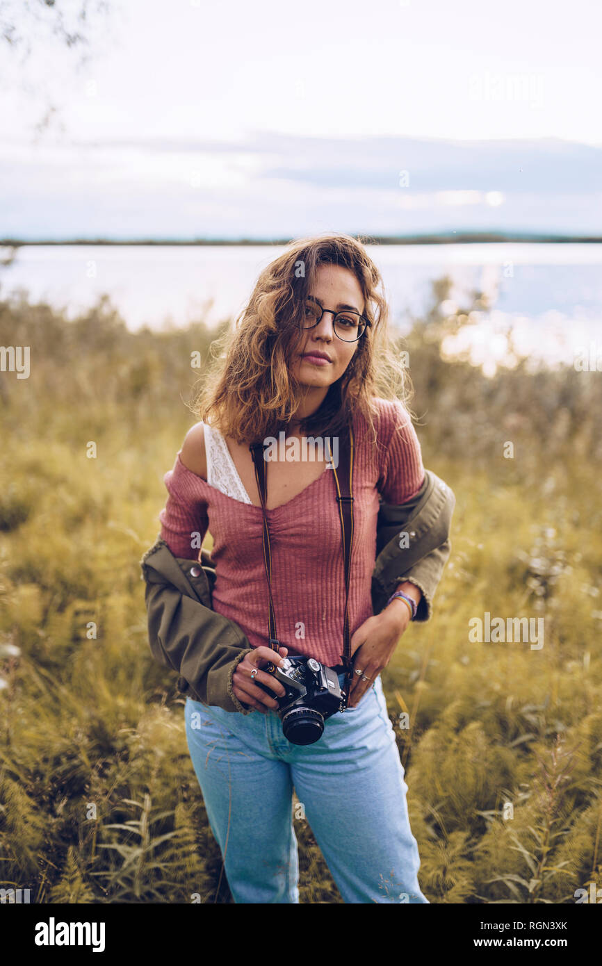 Giovane donna con fotocamera permanente al lago Foto Stock