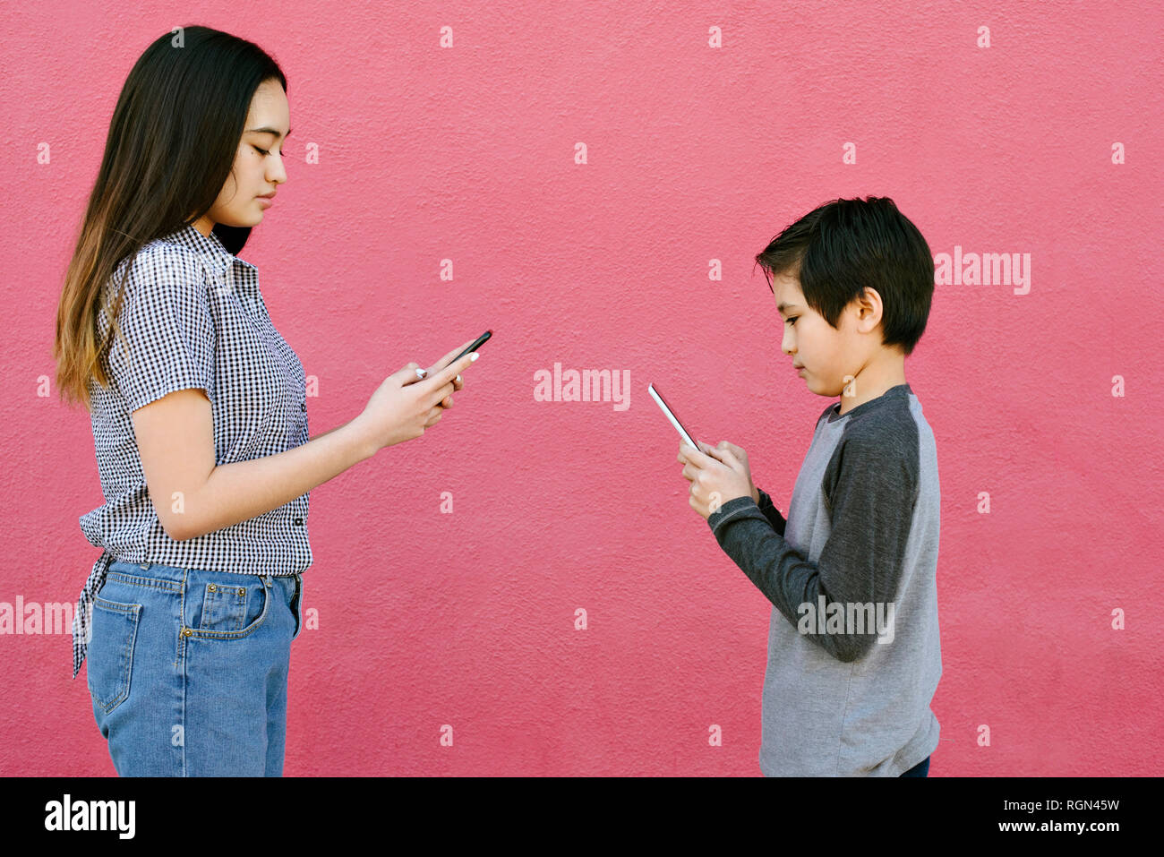 Un fratello e una sorella testo ad ogni altro su smart phone pur essendo allinterno distanza uno dall'altro Foto Stock