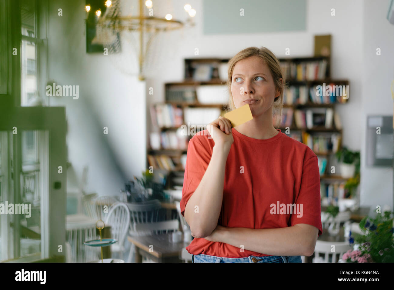 Giovane donna tenendo la scheda in un cafe pensando Foto Stock