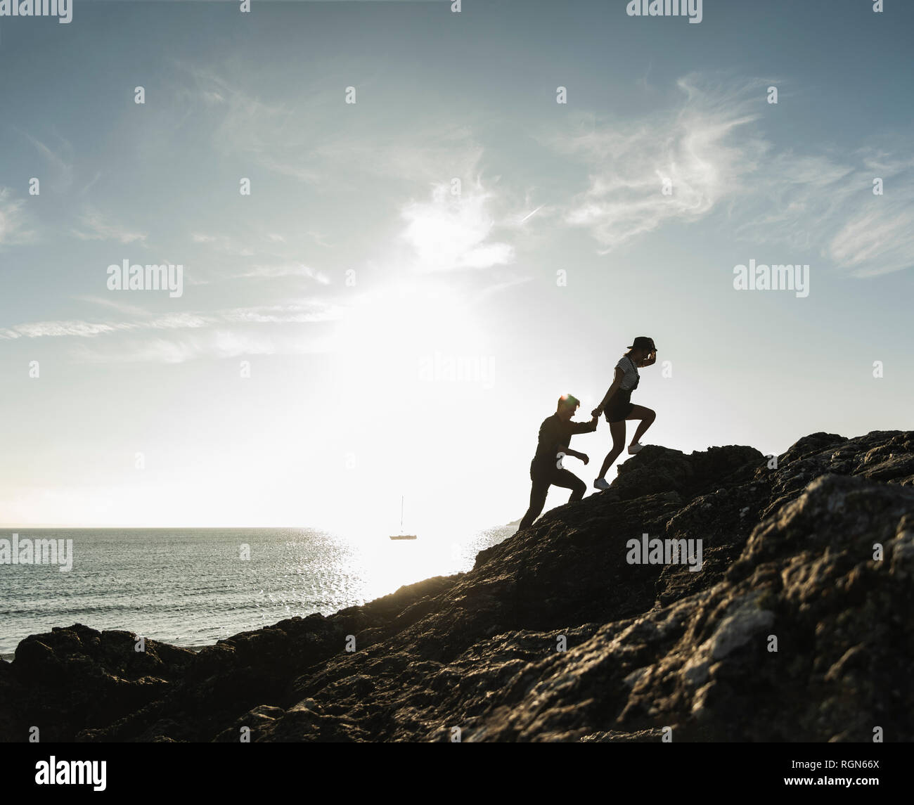 Francia, Bretagna, coppia giovane arrampicata su una roccia sulla spiaggia al tramonto Foto Stock