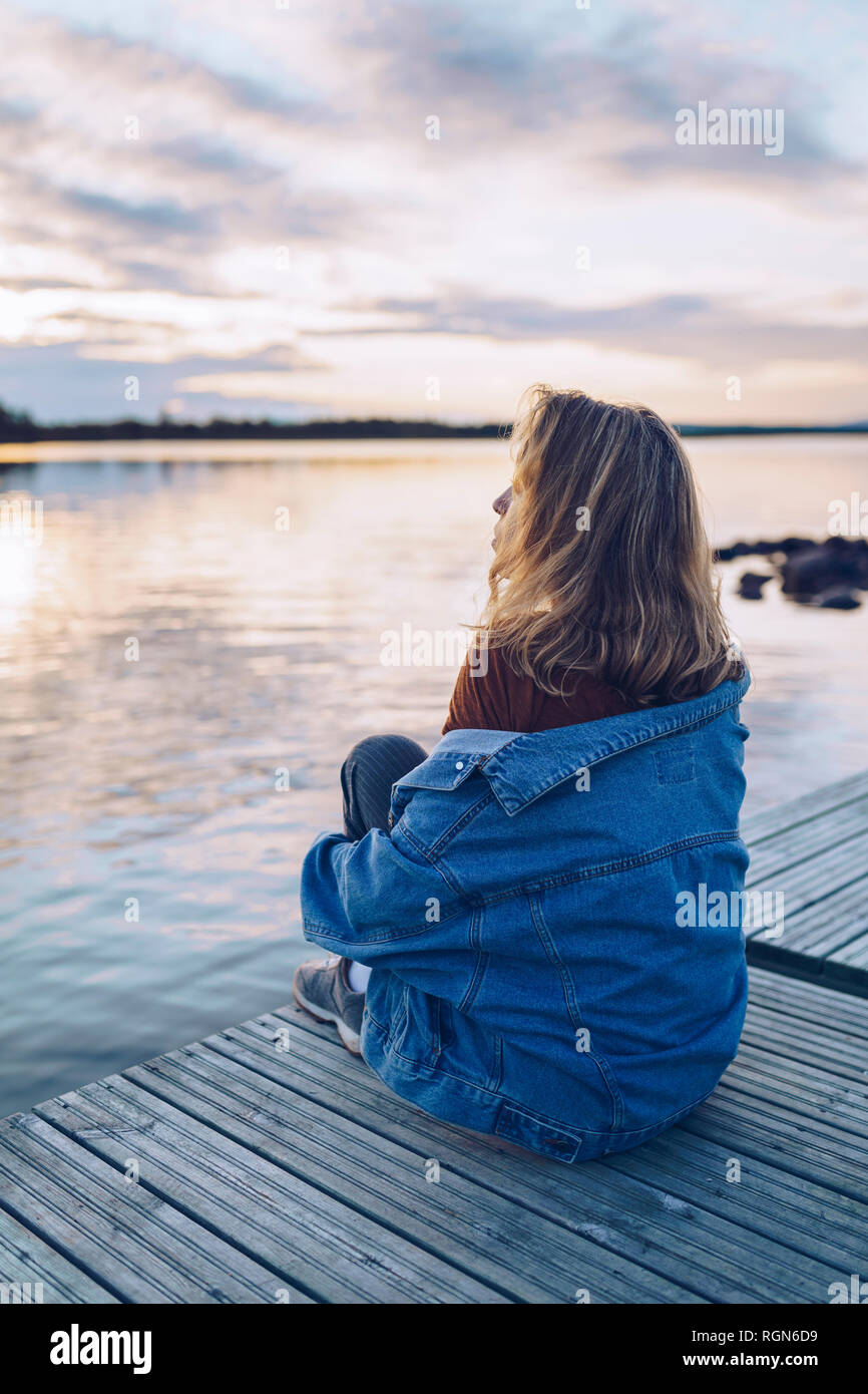 Giovane donna seduta al lago Inari, guardando a vista, Finlandia Foto Stock