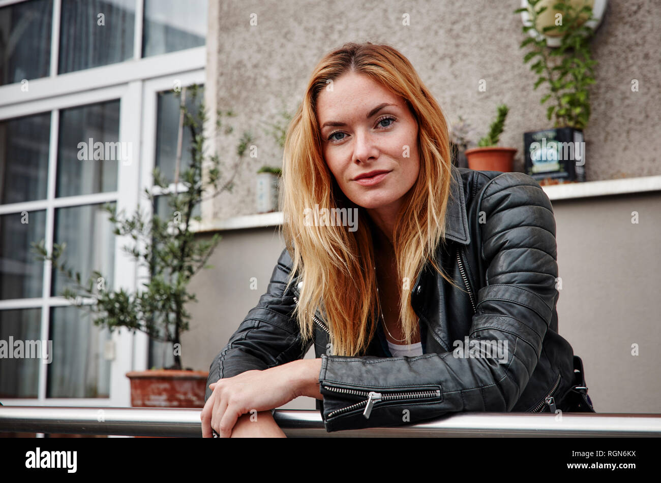 Ritratto di fiducioso giovane donna indossando giacca biker appoggiata sulla ringhiera di balcone Foto Stock