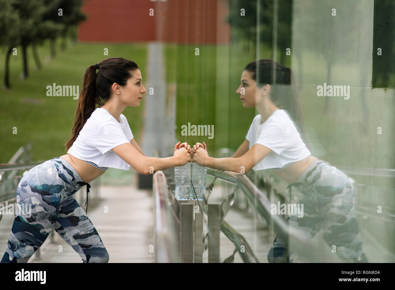 Giovane donna facendo esercizio di stretching riflessa nella facciata di vetro Foto Stock