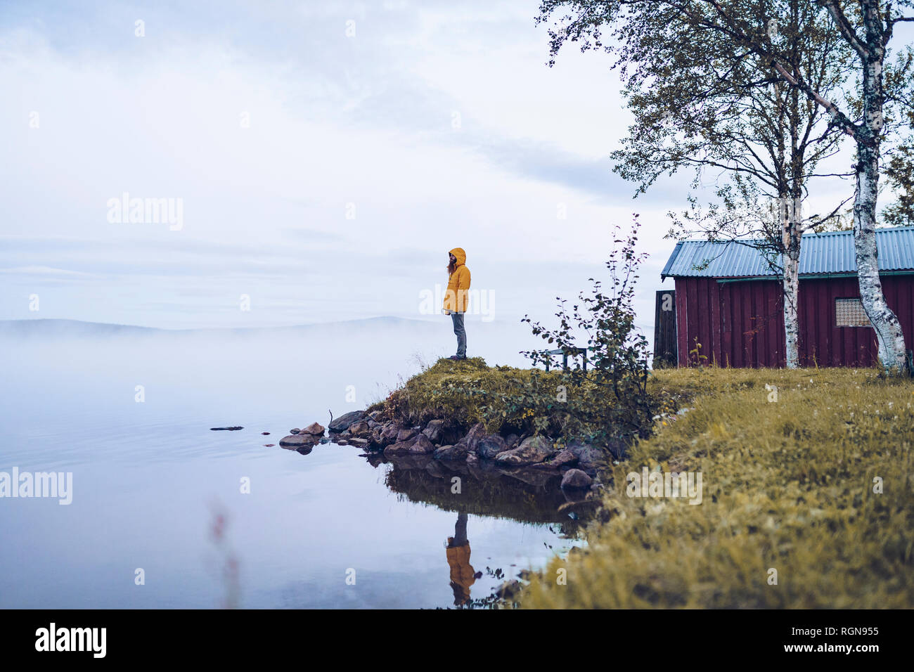 La Svezia, Lapponia, uomo indossando giacca a vento permanente al bordo d'acqua guardando a distanza Foto Stock