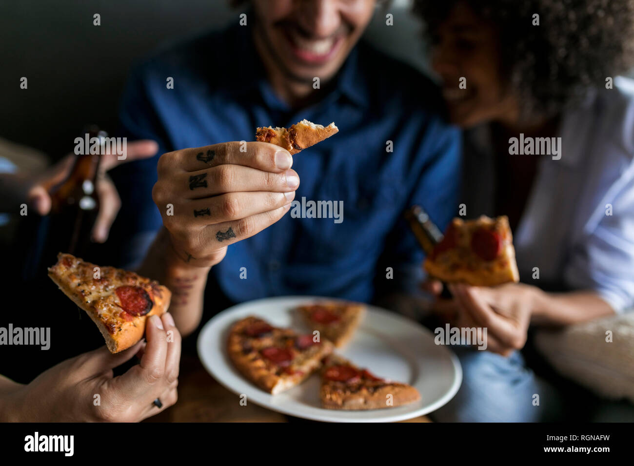 Close-up di tatuati uomo con amici holding trancio di pizza Foto Stock