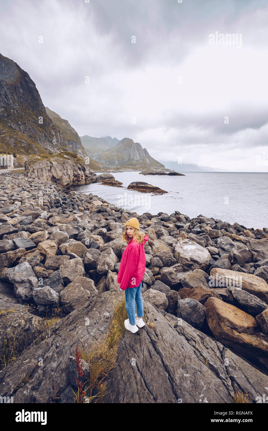 Norvegia Lofoten, giovane donna indossa rainjacket in piedi su una roccia Foto Stock