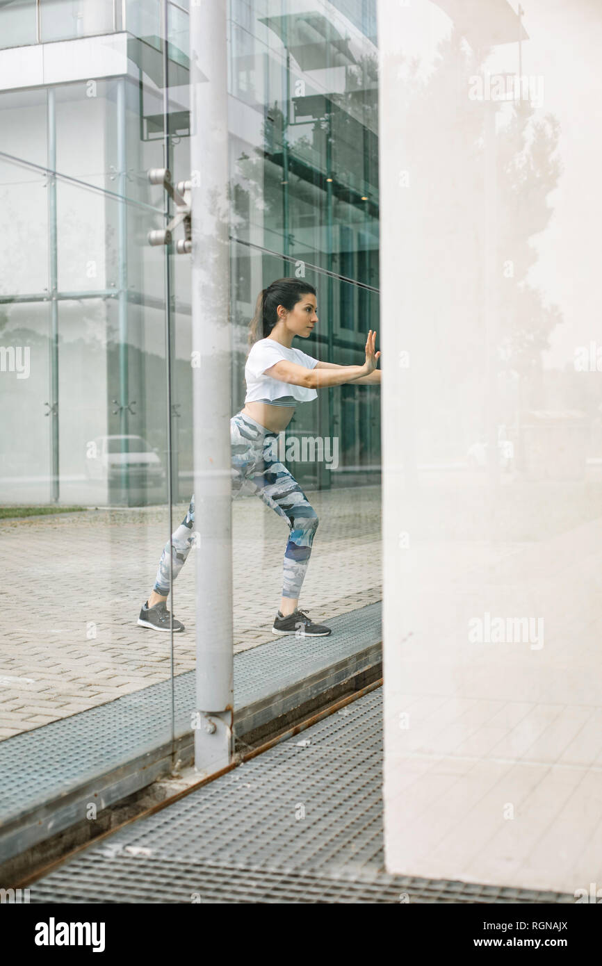 Giovane donna facendo esercizio di stretching alla facciata di vetro Foto Stock