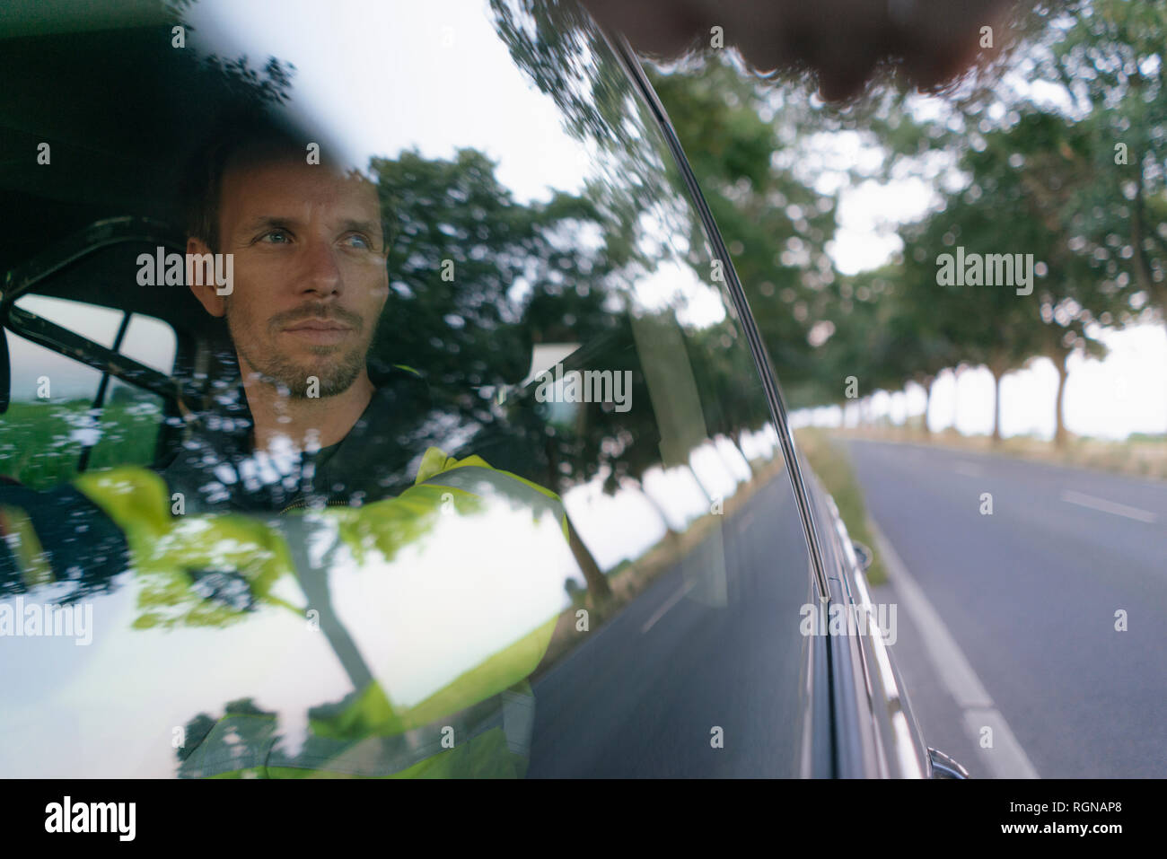 Uomo in indumenti da lavoro protettiva in un auto in strada di campagna Foto Stock