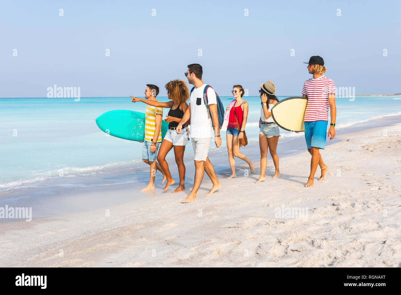 Gruppo di amici di camminare sulla spiaggia, portando le tavole da surf Foto Stock