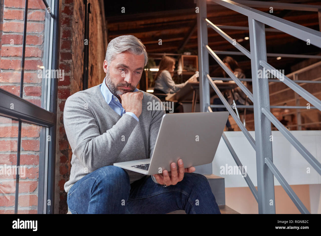Imprenditore seduti sulle scale del moderno ufficio, con il computer portatile Foto Stock