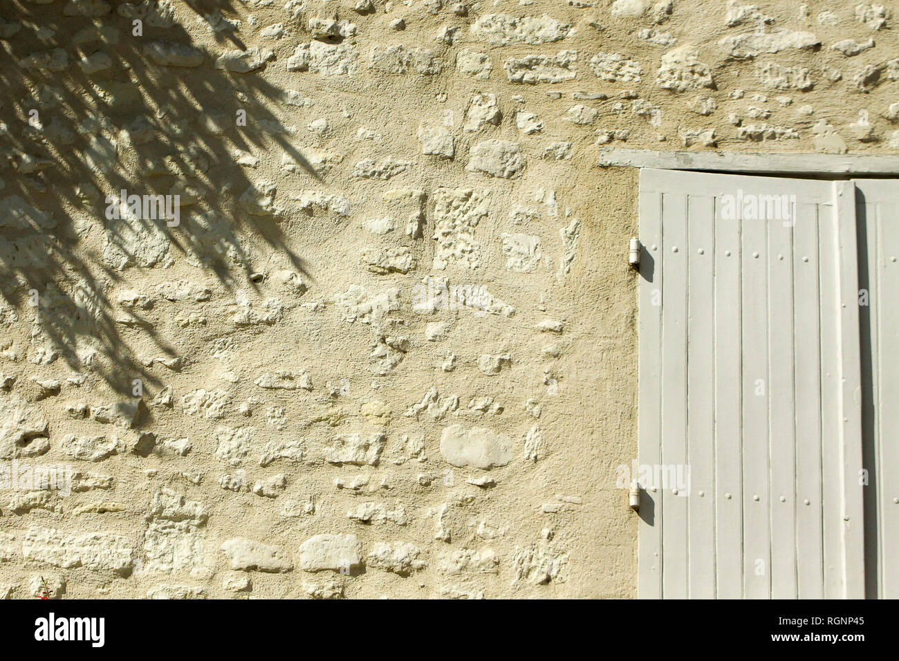 Dettaglio della soleggiata vecchio muro di pietra con persiane e ombre, Francia Foto Stock