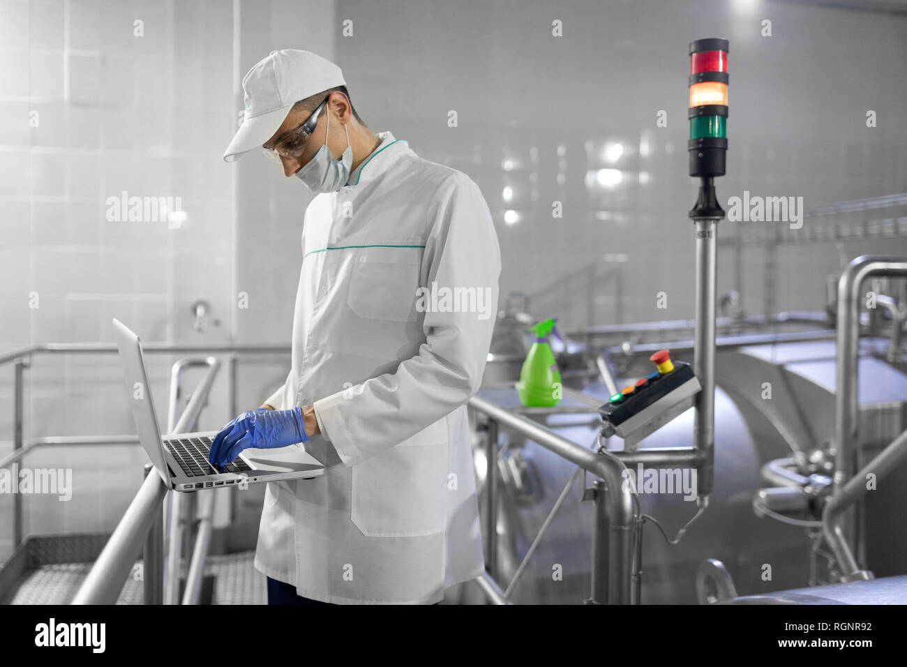 Uomo in una tunica bianca e una maschera con un laptop nelle sue mani è in fabbrica Foto Stock