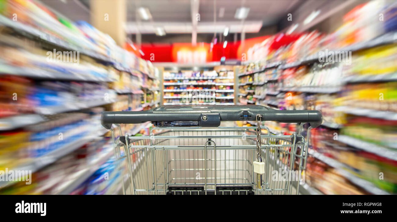 Un vuoto Carrello spesa tra ripiano righe nel supermercato con motion blur. Foto Stock