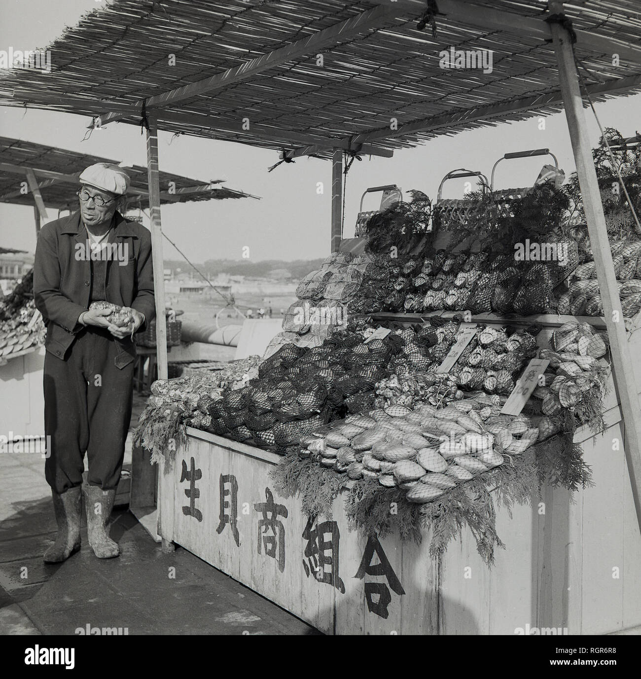 Degli anni Cinquanta, storico, Giappone, pesce stallo, stallholder maschio in piedi dal suo open-air di stallo all'aperto. Foto Stock