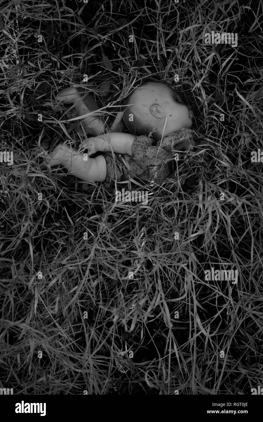 Plastica bruciata creepy bambola giocattolo antico nei boschi. In bianco e nero. Foto Stock