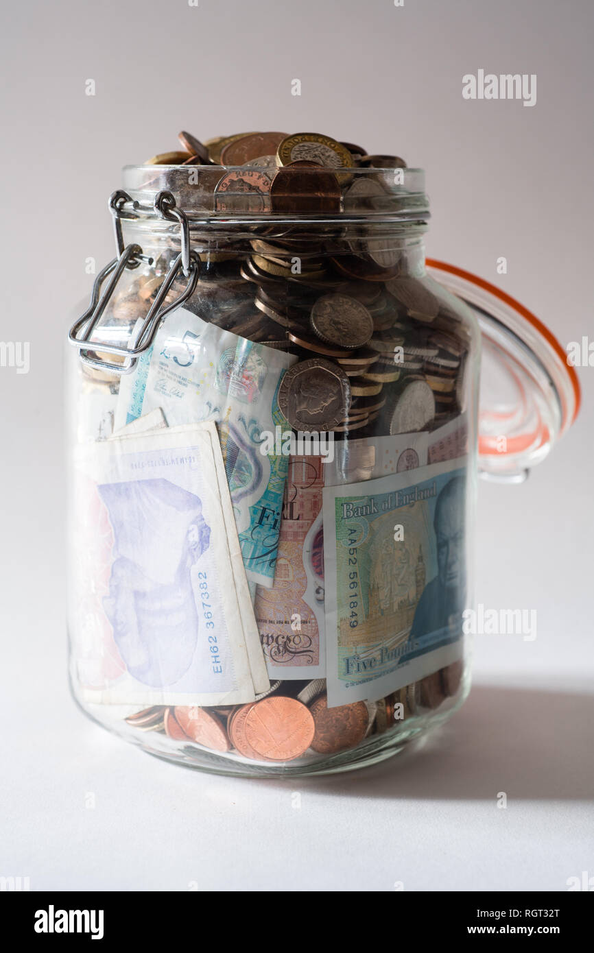 Risparmi REGNO UNITO - un vetro vaso di storage completamente pieno di british delle monete e delle banconote, salvati fino. Concetto illustrazione per la pianificazione previdenziale, giornata piovosa fondo di fondi di emergenza, home banking, in contanti, ricchezza accumulata Foto Stock