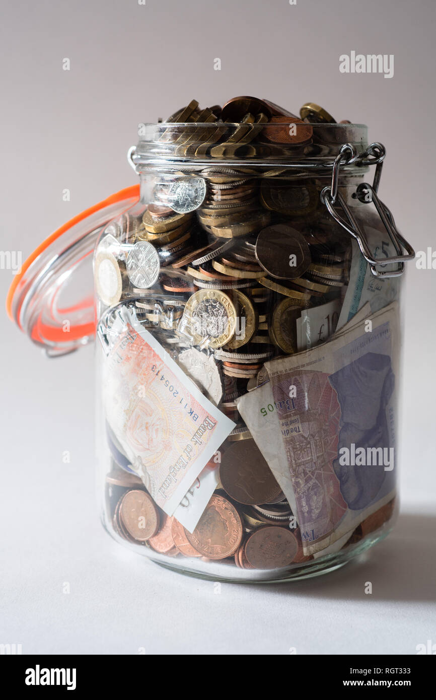 Risparmi REGNO UNITO - un vetro vaso di storage completamente pieno di british delle monete e delle banconote, salvati fino. Concetto illustrazione per la pianificazione previdenziale, giornata piovosa fondo di fondi di emergenza, home banking, in contanti, ricchezza accumulata Foto Stock