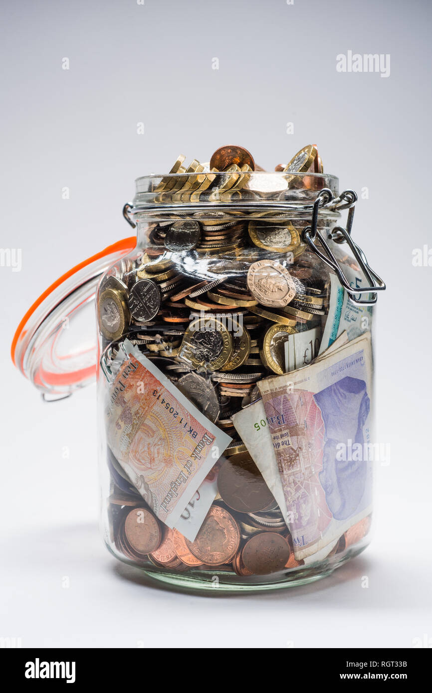 Risparmi REGNO UNITO - un vetro vaso di storage completamente pieno di british delle monete e delle banconote, salvati fino. Concetto illustrazione per la pianificazione previdenziale, giornata piovosa fondo di fondi di emergenza, home banking, in contanti, ricchezza accumulata Foto Stock