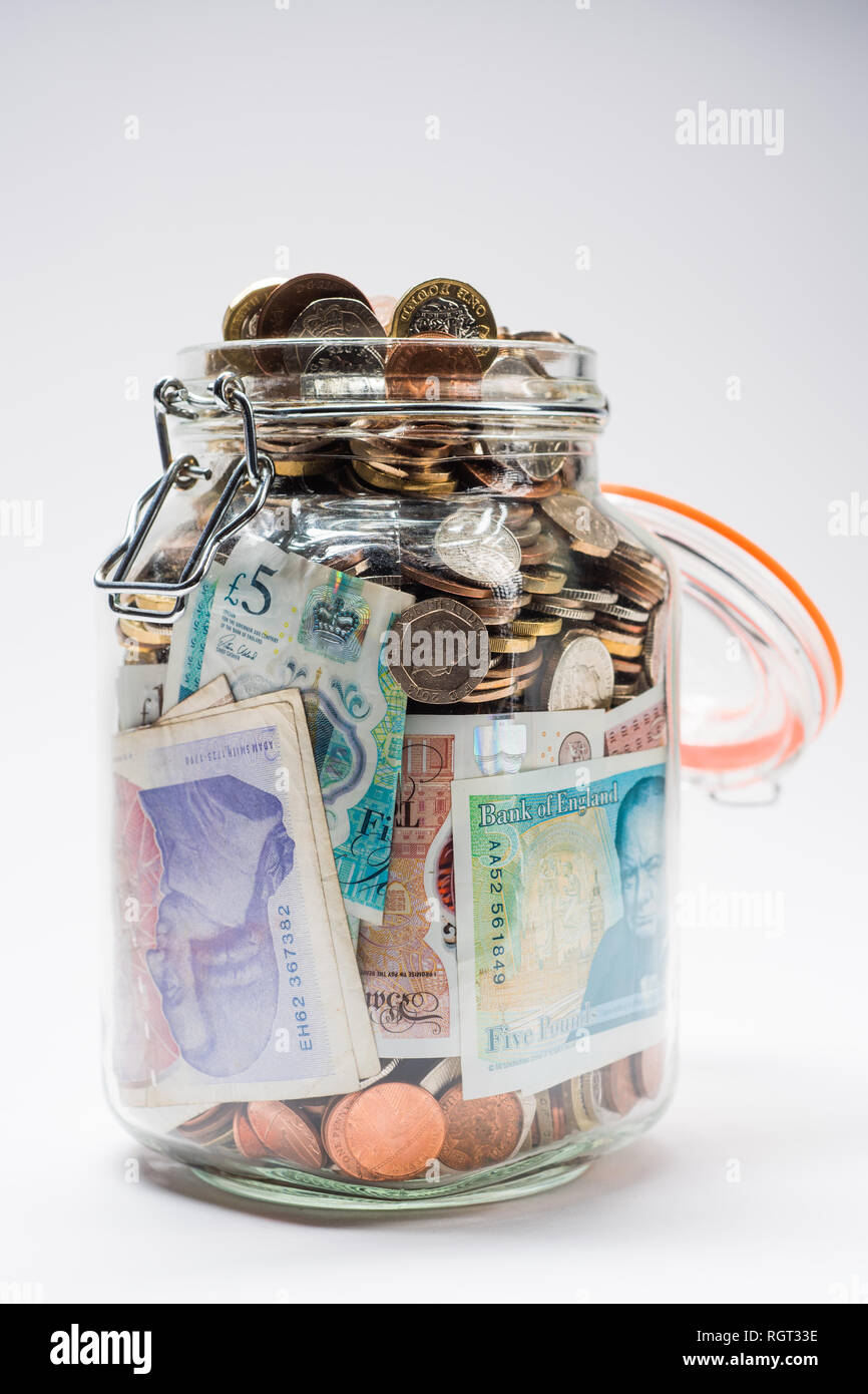 Risparmi REGNO UNITO - un vetro vaso di storage completamente pieno di british delle monete e delle banconote, salvati fino. Concetto illustrazione per la pianificazione previdenziale, giornata piovosa fondo di fondi di emergenza, home banking, in contanti, ricchezza accumulata Foto Stock