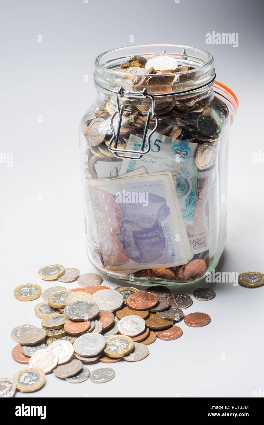 Risparmi REGNO UNITO - un vetro vaso di storage completamente pieno di british delle monete e delle banconote, salvati fino. Concetto illustrazione per la pianificazione previdenziale, giornata piovosa fondo di fondi di emergenza, home banking, in contanti, ricchezza accumulata Foto Stock