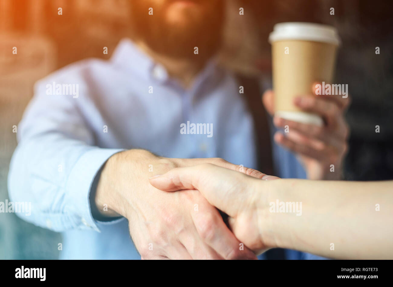 Imprenditore beve caffè e saluta la mano con un partner. Un incontro barba maglietta blu bicchiere di carta stretta di mano incontro di saluto. Pausa caffè Concept Foto Stock