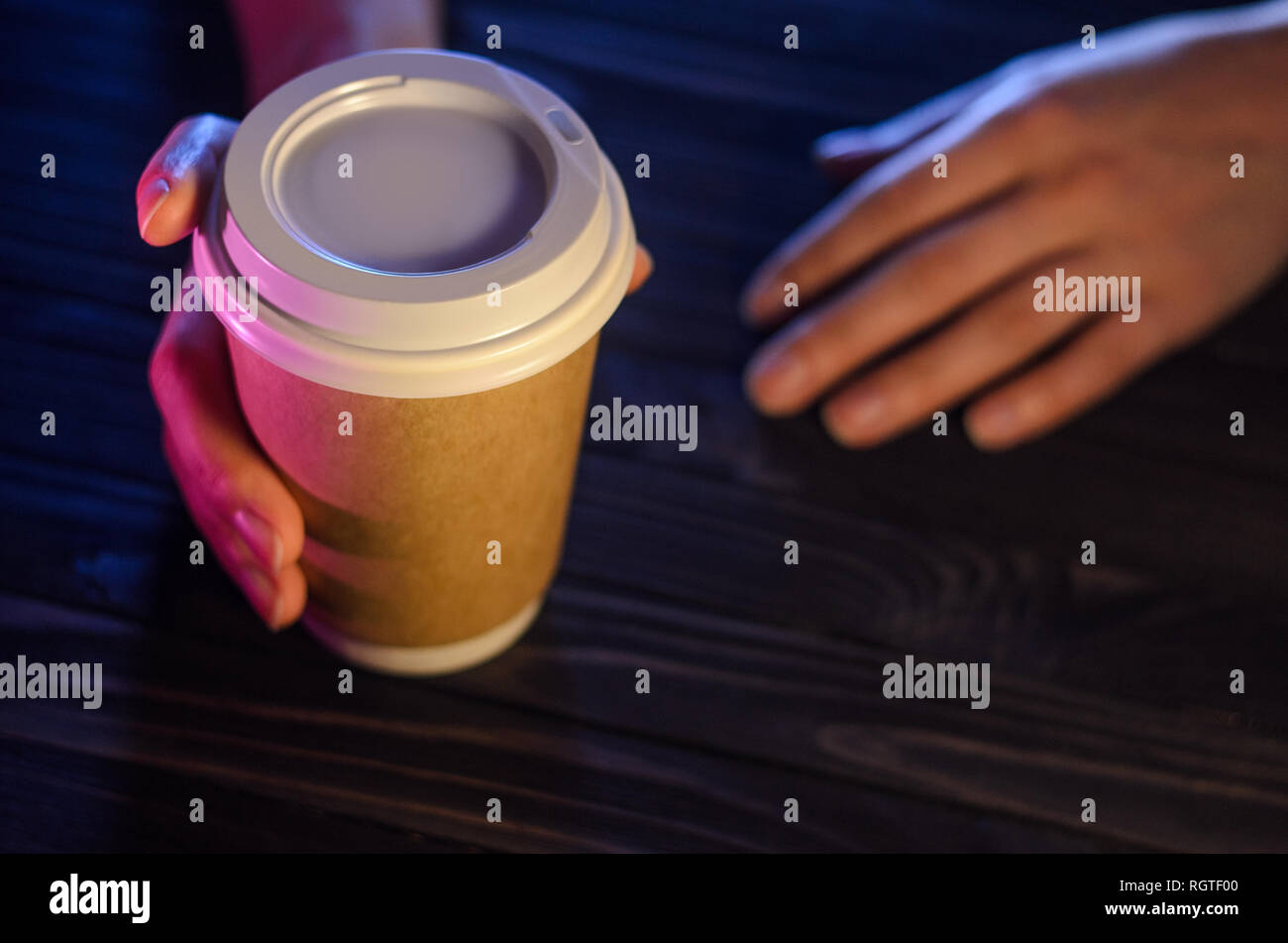 Una tazza di caffè su una tavola di legno in mani femminili. Bicchiere di carta il cappuccio di plastica mani belle ragazza bar luce del contatore Foto Stock