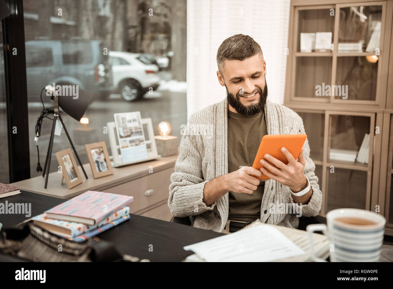 Positivo sorridente ragazzo con barba lussureggiante osservando le informazioni sullo smartphone Foto Stock