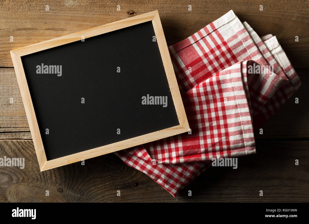 Vuoto, vuoto, lavagna nera con rosso a scacchi canovaccio piatta da laici al di sopra su marrone tavolo in legno con spazio di copia Foto Stock