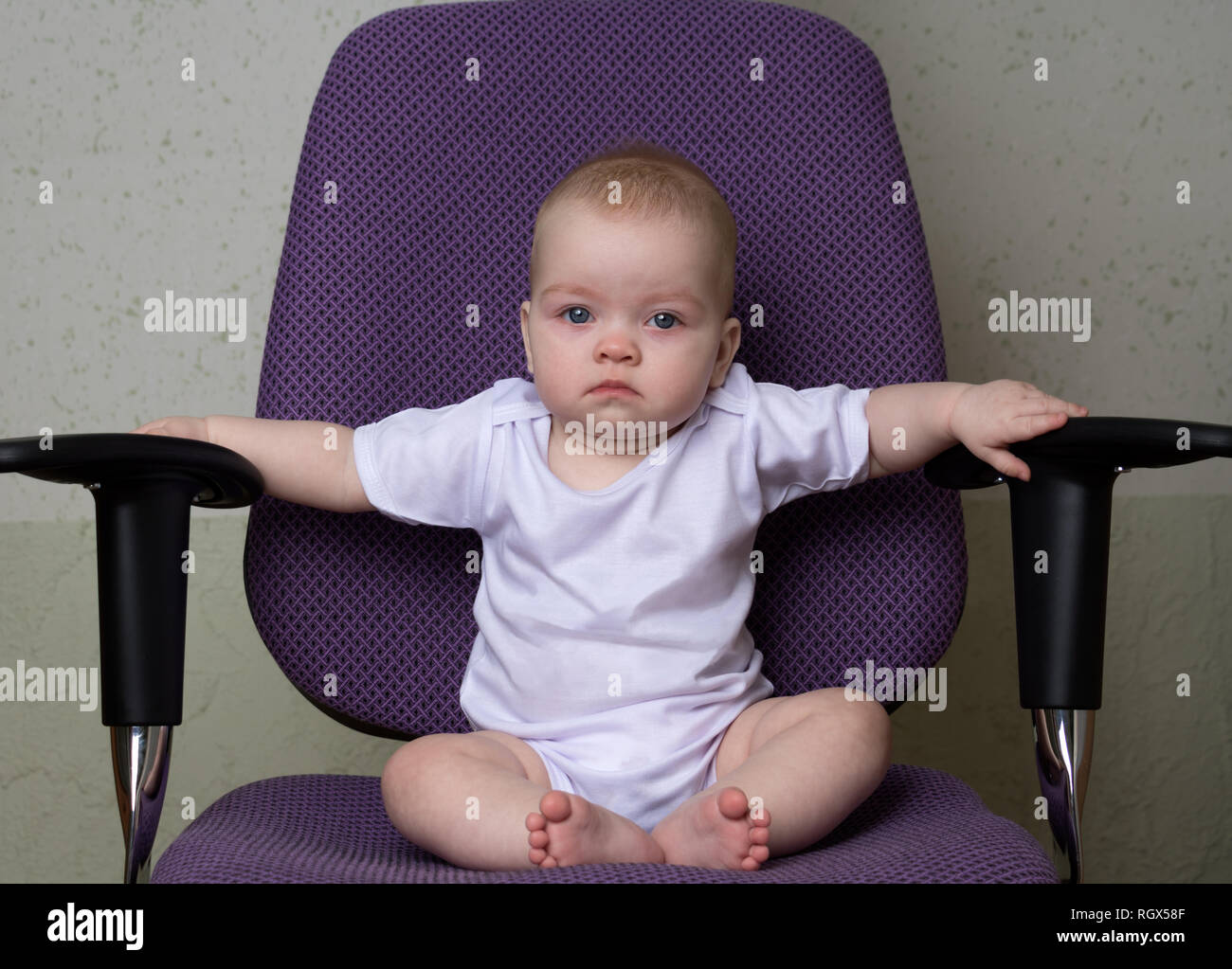 Stanco bambino seduto sulla sedia da ufficio guardando dritto, tenendo il bracciolo Foto Stock