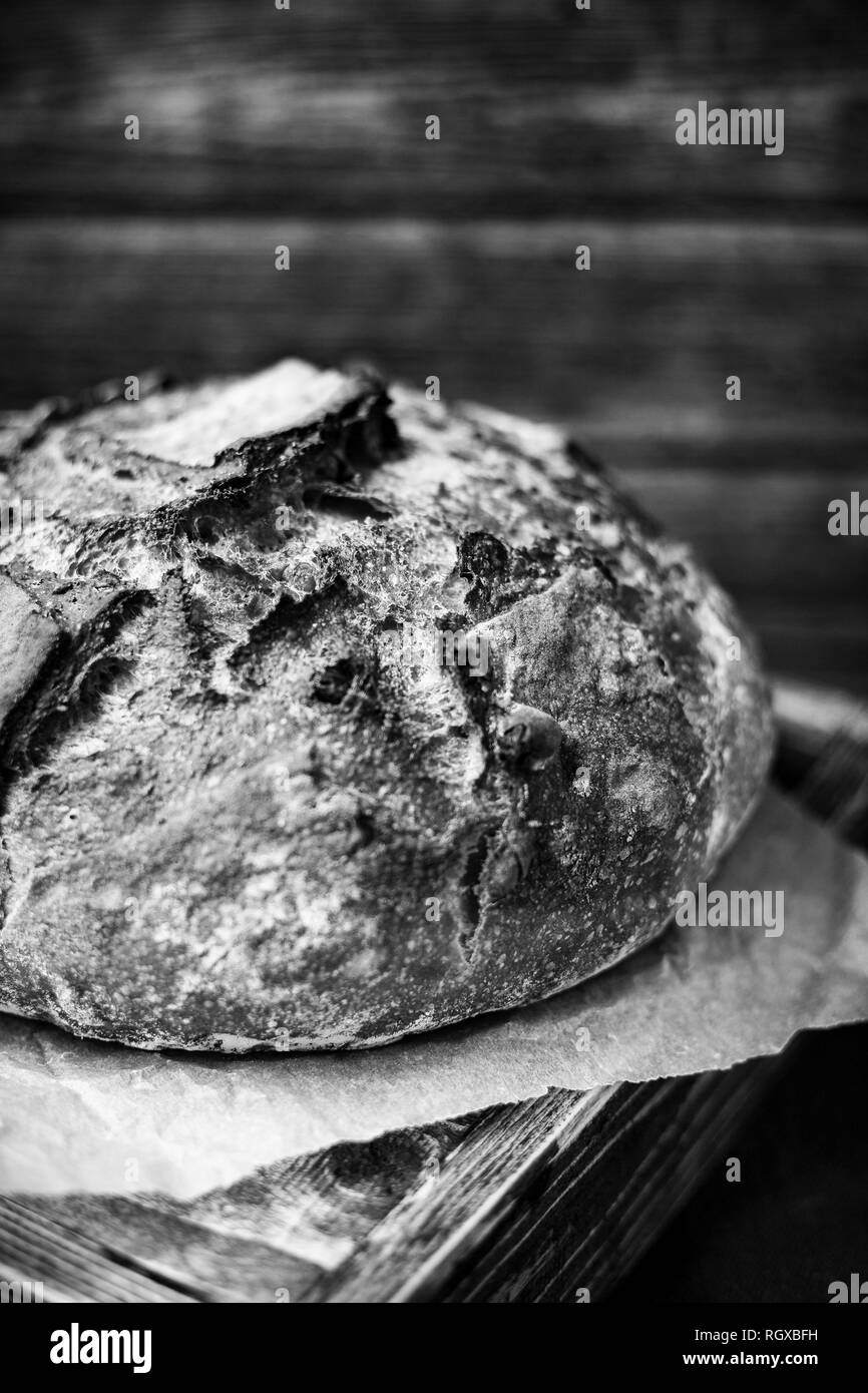 Una pagnotta di pane la posa su un tavolo, su un tavolo con una parete in legno dietro di esso, in bianco e nero, monocromatiche. Foto Stock