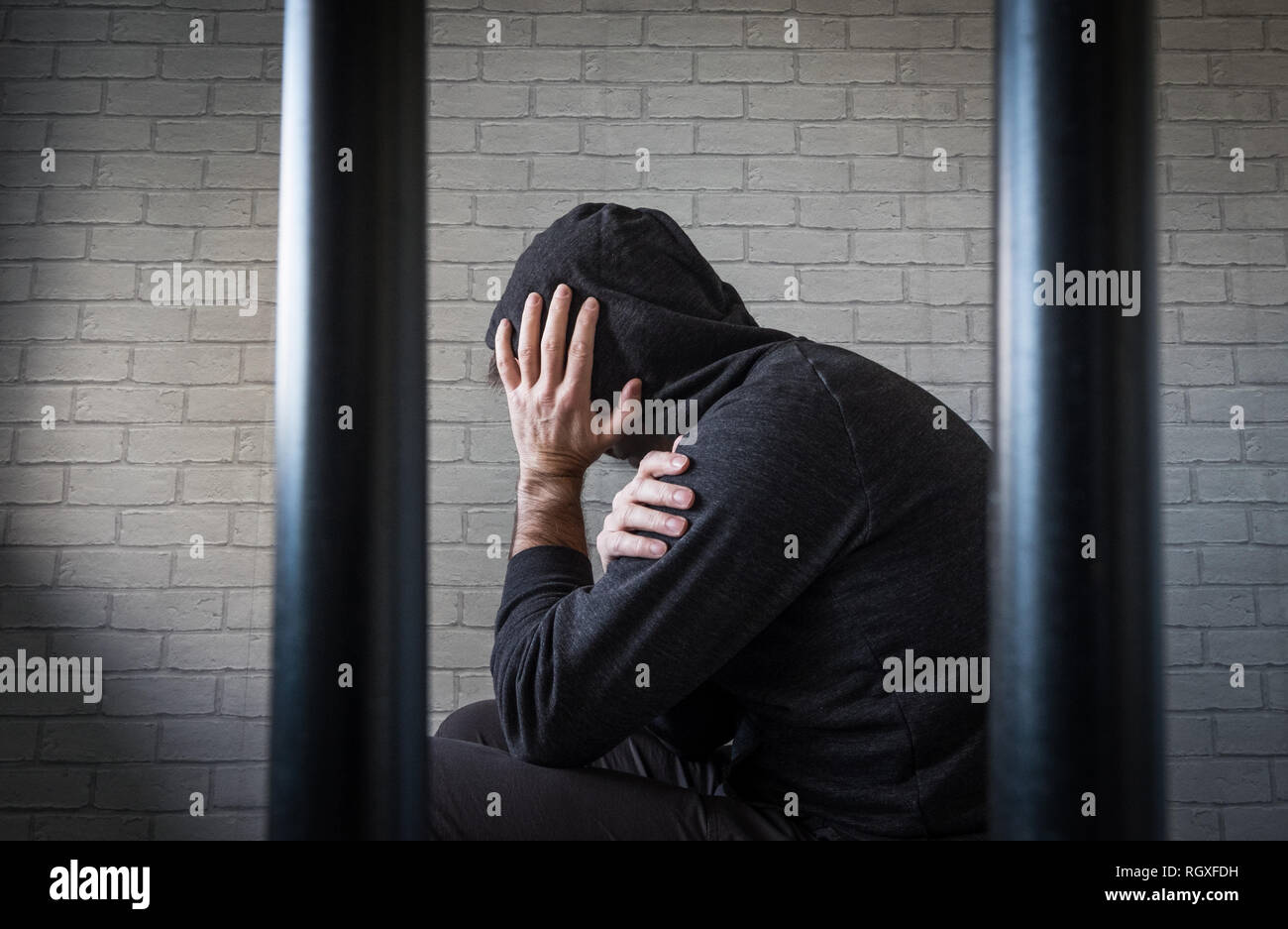 Un prigioniero con la testa tra le mani dietro le sbarre di una cella di prigione (foto poste dal modello) Foto Stock