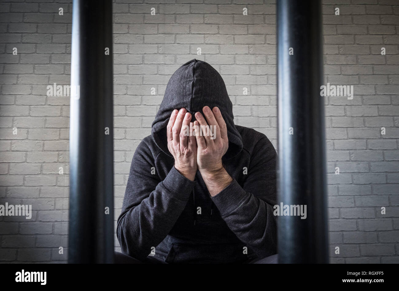 Un prigioniero con la testa tra le mani dietro le sbarre di una cella di prigione (foto poste dal modello) Foto Stock