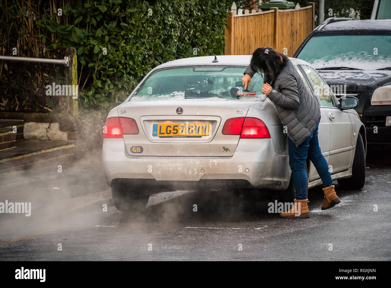 Reigate, Regno Unito - 30 Gennaio 2019 - Una donna raschiando il ghiaccio dal finestrino dell'auto in una fredda mattina di inverno Foto Stock