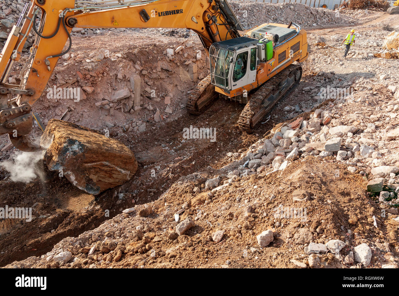 Decostruzione sito. Un Liebherr 954 escavatore, con un dente ripper, estrae un grande blocco di cemento residue dalle fondamenta di un edificio. Foto Stock