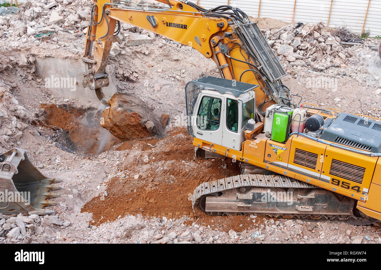 Decostruzione sito. Un Liebherr 954 escavatore, con un dente ripper, estrae un grande blocco di cemento residue dalle fondamenta di un edificio. Foto Stock